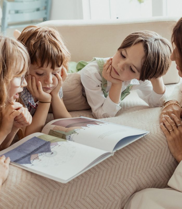bambini leggono un libro sul divano con le loro babysitter vicine